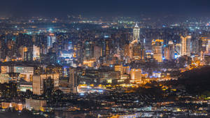 夜晚密集燈光的城市天際線景觀，高聳的建築物和發光的街道。 — 城市燈光 壁紙