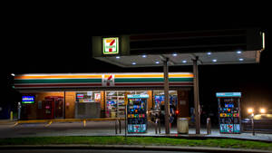 夜晚照明的7-Eleven加油站，可見油泵和店面。 — 瓦斯 壁紙
