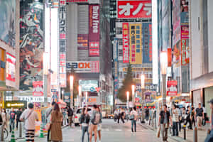 夜晚東京擁擠的街道，閃爍的霓虹燈牌和動漫廣告看板。 — MacBook Pro M4 壁紙