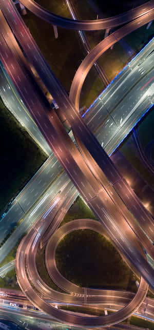 複雜高速公路交流道的夜間空拍圖，有發光的行車道和行駛中的車輛。 — 小米18 Pro Max 壁紙