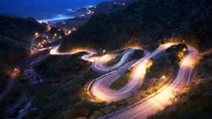 夜晚蜿蜒的海岸道路，帶有移動汽車的發光車燈軌跡。 — 光線 壁紙
