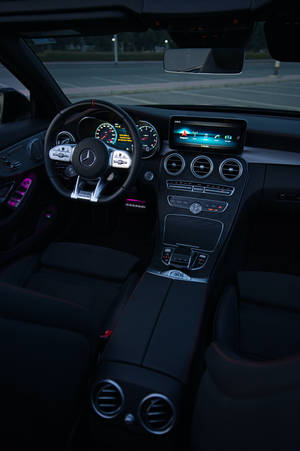 黑色豪華車內裝，帶有發光數位顯示屏和環境紫色燈光。 — Mercedes Amg iPhone 壁紙