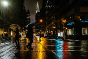 行人撐傘在發光的霓虹招牌下，走過夜晚雨濕的城市街道。 — 城市燈光 壁紙