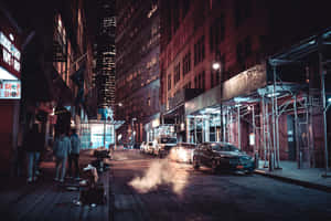 夜晚的城市街道，有行人、停放的汽車和照亮的建築物。 — 街頭 壁紙