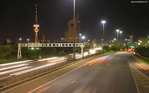 夜間城市高速公路，有行駛汽車的光跡和發光塔。 — 科威特 壁紙