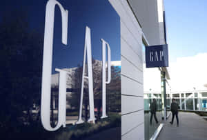 GAP商店外觀，大型白色字母反射天空和樹木，行人走過。 — 間隙 壁紙
