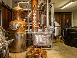 在質樸的工作坊中，銅和不鏽鋼蒸餾設備與香草籃。 — 品牌 壁紙