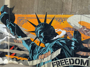 塗鴉壁畫，描繪自由女神像手持火炬和刻有「FREEDOM」橫幅的石板，位於混凝土牆上。 — 街頭藝術 壁紙