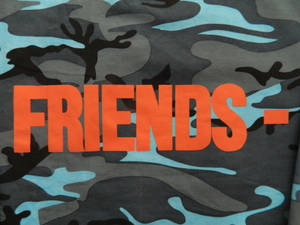 橙色「FRIENDS」文字在迷彩布料上的特寫。 — Vlone 壁紙