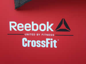 Reebok CrossFit標誌在紅色牆上，上方有一個深色布料角落。 — 銳步 壁紙