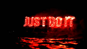 紅色LED標誌寫著JUST DO IT，在夜晚發光，並在濕地上反射。 — 就去做吧 壁紙
