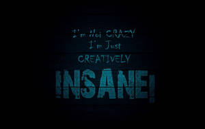 深色木材上的藍色塗鴉風格文字寫著「I'm Not Crazy I'm Just Creatively Insane!」。