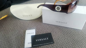 Versace 太陽眼鏡連同眼鏡盒及保固卡放在灰色布料上。 — 凡賽斯 壁紙