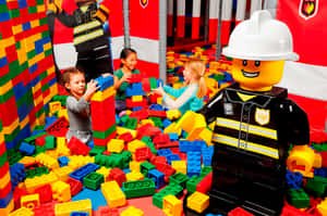 孩子們在LEGO消防員人偶旁邊玩LEGO積木。 — 樂高 壁紙