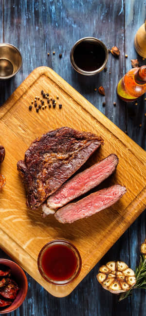 切片 medium-rare 牛排，配大蒜、迷迭香和醬汁，置於木板上。 — Galaxy A54 壁紙