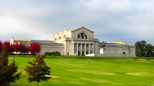 大型博物館建築，帶有柱子和雕像，位於長滿紅樹和散步人群的草坡上。 — 博物館 壁紙