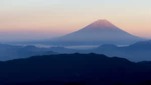 黎明時分的富士山，層疊山巒輪廓之上有粉紅色和藍色的天空。