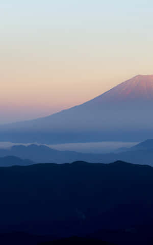 黎明時分的富士山，層疊山巒輪廓上空有粉紅色和藍色的天空。 — 乾淨 壁紙