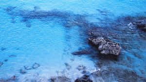 綠松石色海水從上方流過深色火山岩周圍。 — 藍色美學電腦 壁紙