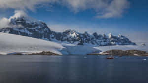 帆船在冰雪覆蓋的南極水域中漂流，背景是白雪皚皚的山峰。 — 南極洲 壁紙