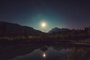 月光倒映在被山脈和樹木環繞的湖面上，星空下。 — 高畫質月亮 壁紙