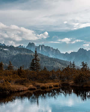 山湖映照鋸齒狀山峰和秋日樹木，天空多雲 — 湖泊 壁紙