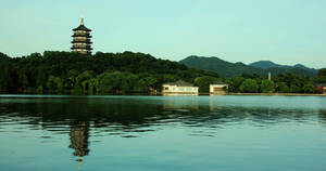 寶塔倒映在平靜的湖面上，四周環繞著翠綠的山丘和傳統建築。 — 唐人街 壁紙