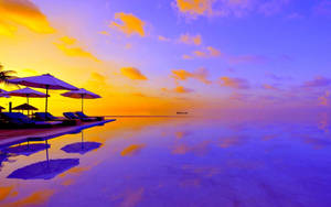 日落時的無邊際泳池，躺椅和遮陽傘倒映在平靜的水面上。