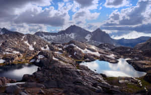 高山湖泊映照多雲的天空，有積雪的山峰和岩石海岸。 — 秋天 壁紙