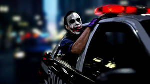 小丑在夜晚的城市中從亮著紅燈的警車中探出身子。 — 小丑 2019 壁紙