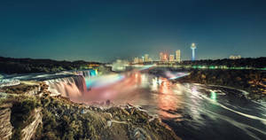 尼亞加拉瀑布在夜間發光，背景是彩虹霧氣和城市燈光。