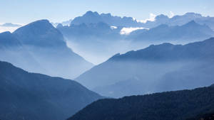 寧靜的山景，藍天下有霧氣籠罩的山谷和森林覆蓋的山坡。 — 丘陵景觀 壁紙