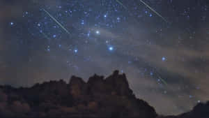 岩石山脈在星空下，有流星劃過。 — 星星 壁紙