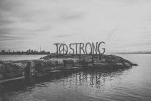 岩石島上「TO STRONG」編織標誌，背景為城市天際線。 — 和平符號 壁紙