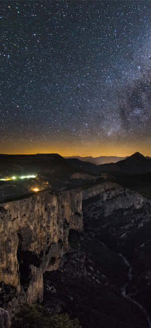 深邃山峽上空的星空與遠處燈光。 — Galaxy S24 FE 壁紙