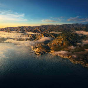 日出時海岸山脈聳立於海面與雲層之上，金色光芒與深藍海水。 — macOS Big Sur 動態桌布 壁紙