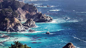 在明亮日光下，崎嶇的海岸懸崖與碧綠的海水和拍岸的浪花。 — 海洋藍 壁紙