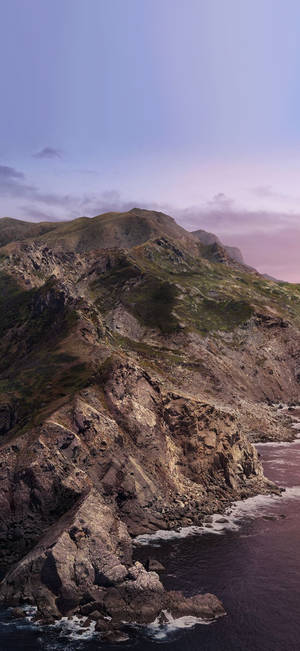 崎嶇懸崖在暮色中與海洋相遇，天空呈現粉紅和藍色 — Pixel 9 Pro 壁紙