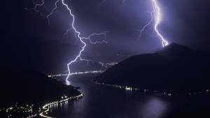閃電劃過黑暗的湖面，沿岸有城市燈光。 — 閃電 壁紙