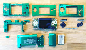 已拆解的綠色 Game Boy Micro 放在木桌上，顯示內部零件。 — 4K 遊戲 壁紙