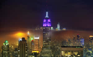 帝國大廈在夜間被紫色照亮，位於閃爍的城市天際線之上。 — 帝國大廈 壁紙