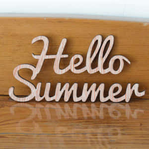 木製 'Hello Summer' 標誌放在帶有反光的木質表面上。 — iPad (A16) 壁紙