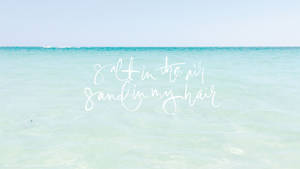 平靜的藍綠色海洋上白色文字寫著 salt in the air sand in my hair。 — 筆電 壁紙