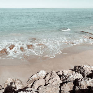 海浪沖刷沙灘，前景有大岩石，天空晴朗 — 土耳其藍 壁紙