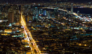 夜間城市景觀，燈火通明的建築物和橫跨水面的燈光橋樑。 — 舊金山 壁紙