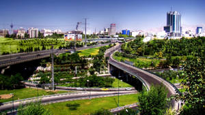 蜿蜒的高速公路穿過綠色公園，背景是現代城市建築。 — 德黑蘭 壁紙
