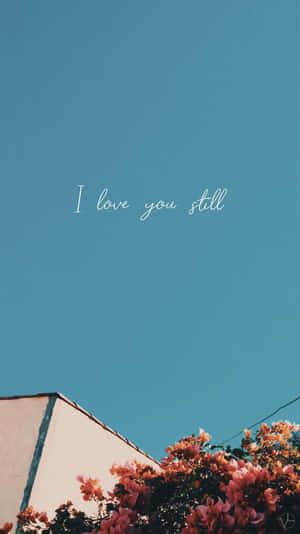 藍天、粉紅色花朵和建築物角落，帶有文字「I love you still」 — 花 iPhone 壁紙