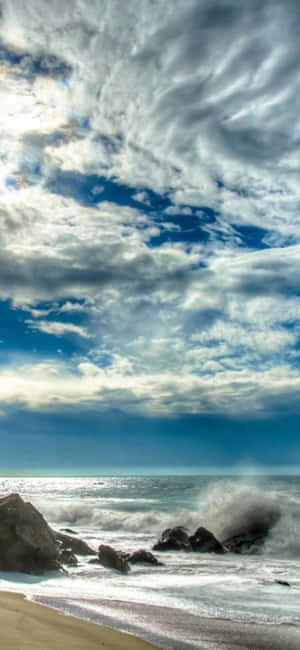 在戲劇性的多雲天空下，海浪拍打著岩石。 — iPhone 17 Pro 壁紙