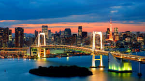 黃昏時分的東京天際線，彩虹橋和東京塔在水面上亮起。 — 16:9 壁紙