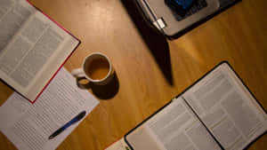 在溫暖燈光下，放有打開的書本、筆記型電腦、咖啡杯和筆的書桌。 — 讀書 壁紙
